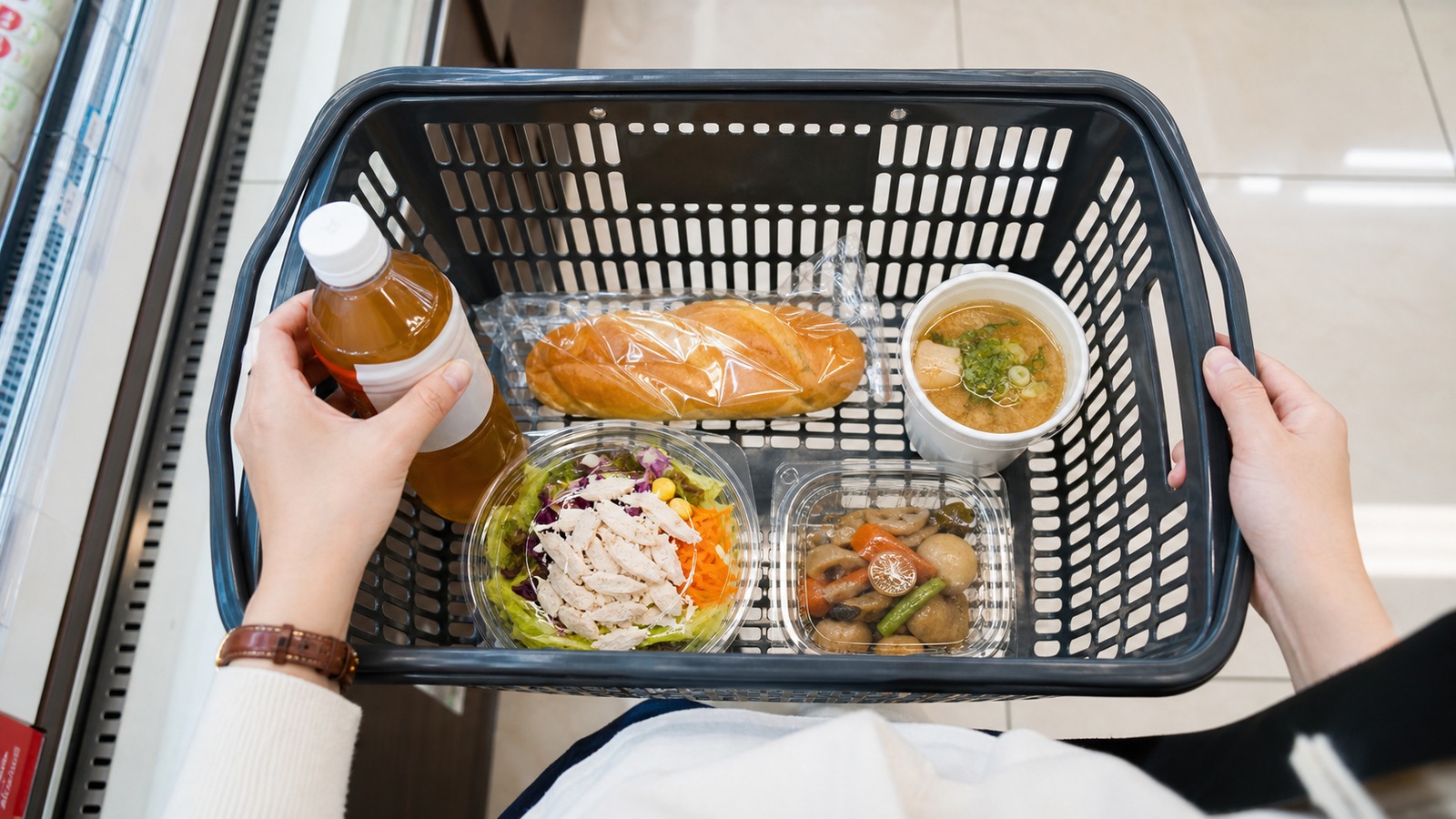コンビニの買い物かごに入れたパン・サラダ・惣菜・飲み物を会計前に確認する様子